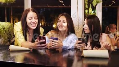 三个漂亮女孩在酒吧看手机上的照片时都在笑